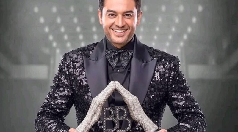 A man in a glittery black suit holding a trophy with "BB" and "Winner Bigg Boss 19" inscribed, smili.
