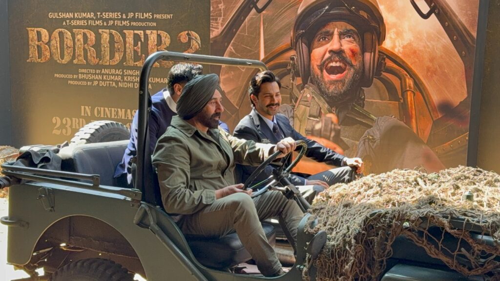 Two men in military attire riding a military vehicle with a fighter jet poster in the background.