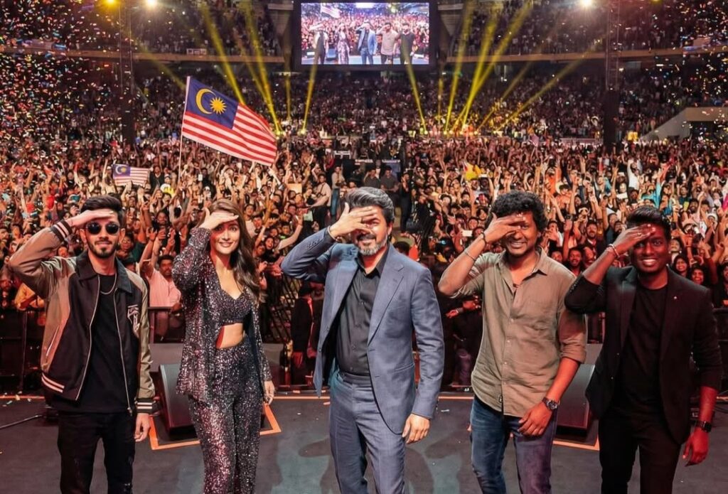 Celebrating at SOOCHNA TANTRA event with a vibrant crowd and Malaysian flag in the background.