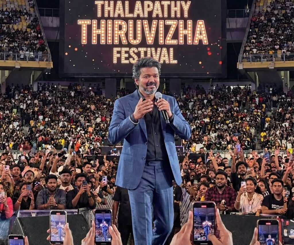 Thalapathy Thiruvizha Festival event with a speaker on stage and large audience in attendance.