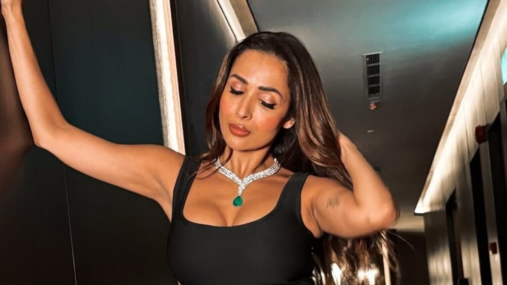 Woman with long hair wearing black dress and jewelry in a modern indoor setting.