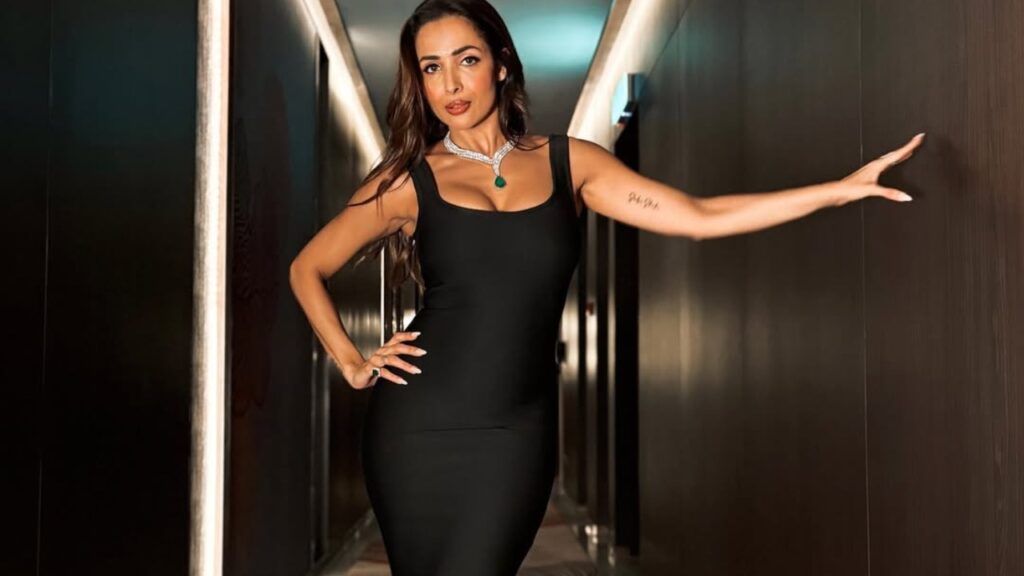 Elegant woman in black dress posing in a modern corridor, showcasing confidence and style.