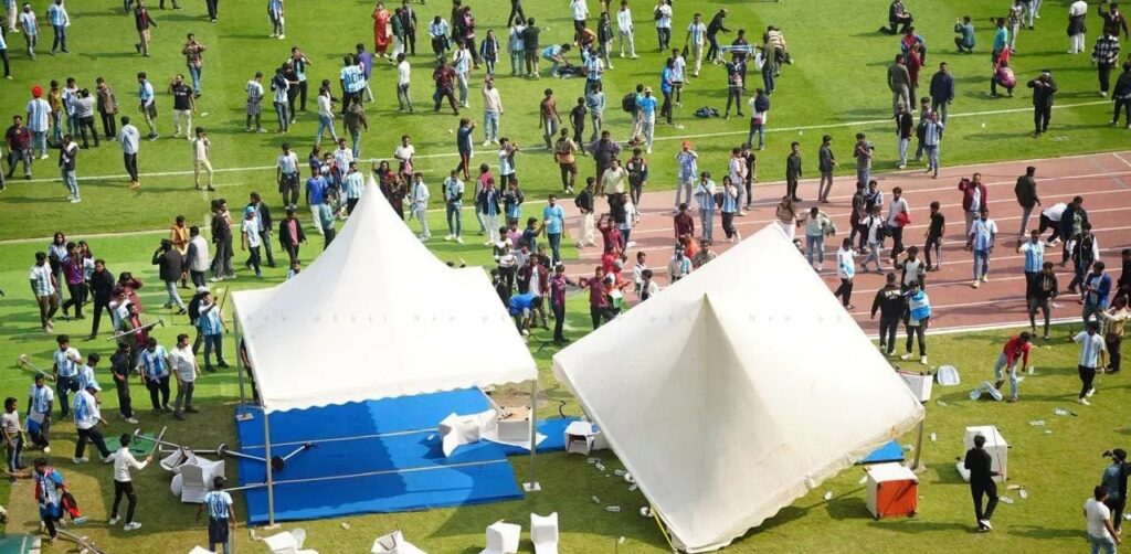 A lush green outdoor event with large white tents and a crowd of people enjoying a community gatheri.