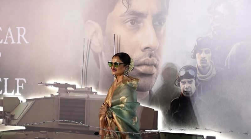 A woman in traditional attire standing in front of a large poster with a man's face and military ima.