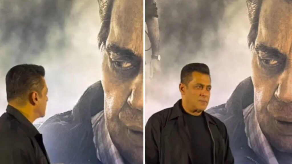 A man in a black jacket looking at a large poster of a serious man's face.