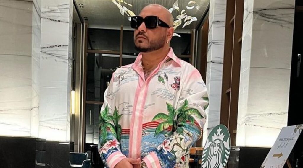 A man wearing sunglasses and a colorful tropical print shirt at a modern indoor location.