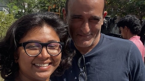 A woman smiling with glasses and a man outdoors, both appearing happy and engaged.