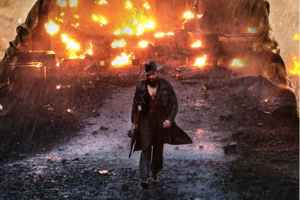 A fiery explosion in the background with a person walking away, symbolizing chaos and destruction.