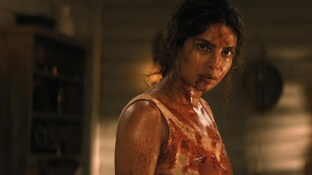 A woman covered in blood, looking intense and focused in a dimly lit setting.