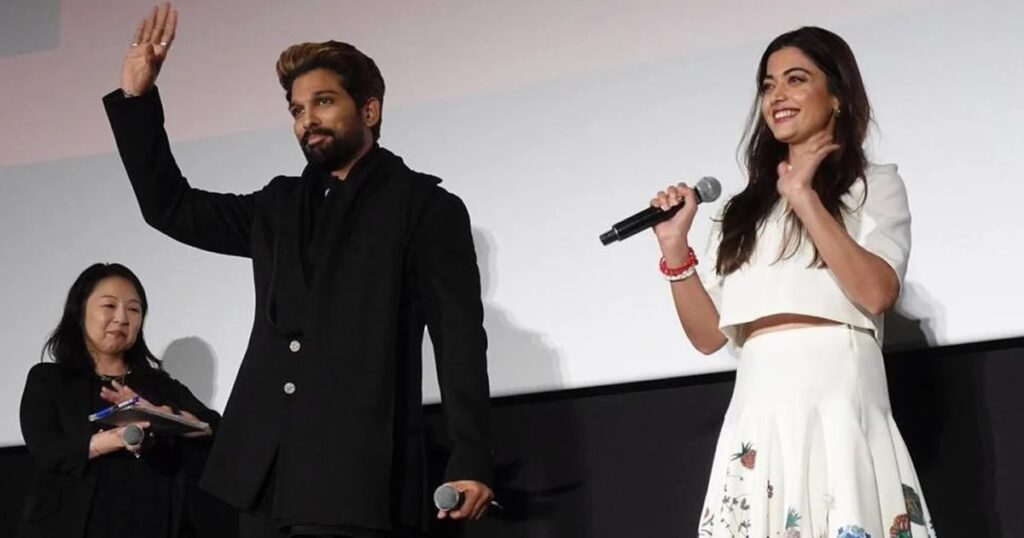 A woman and a man on stage, woman holding a microphone, at a public event or presentation.